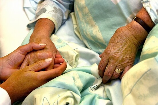 Zwei Hände halten die Hand einer Patientin im Bett.