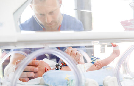 Arzt hört mit dem Stethoskop ein Neugeborenes im Inkubator ab