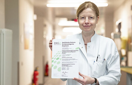 Prof. Dr. Jordan im Flur einer Station mit dem Zertifikat der Deutschen Krebsgesellschaft "Zertifiziertes Zentrum für Hämatologische Neoplasien"