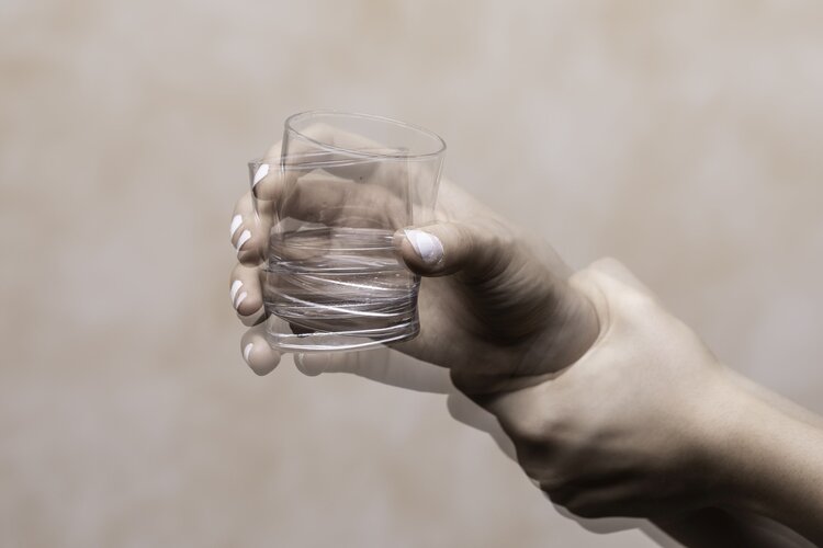 Zitternde Hände halten ein Glas Wasser.