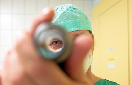 Mitarbeiter der Zentralen Sterilgutversorgung schaut mit dem Auge durch ein Endoskop