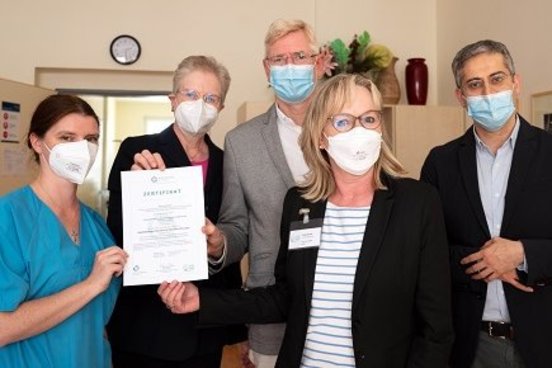 Das Gruppenbild zeigt fünf Personen bei der Übergabe des Zertifikats von Frau KAtja Rothe (GeriZert) an das Team der Geriatrie
