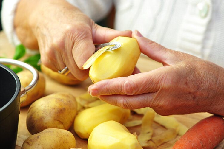 Weibliche Hände schälen eine Kartoffel