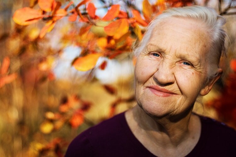 Portrait einer lächelnden Seniorin vor einem herbstlich bunten Hintergrund