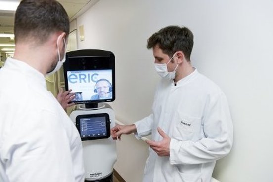 Zwei Ärzte mit einem Visitenroboter bei einer telemedizinischen Visite auf einer Intensivstation.