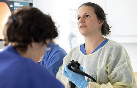 Ärztin blickt auf einen Monitor während einer endoskopischen Untersuchung, zwei Pflegekräfte an ihrer Seite