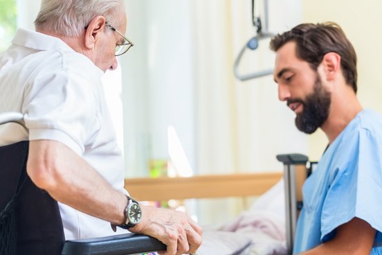 Altenpfleger spricht mit einem Patienten im Rollstuhl
