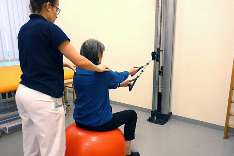 Physiotherapeutin unterstützt eine Patientin beim Übungen zur Kräftigung der oberen Extremität und des Rumpfes