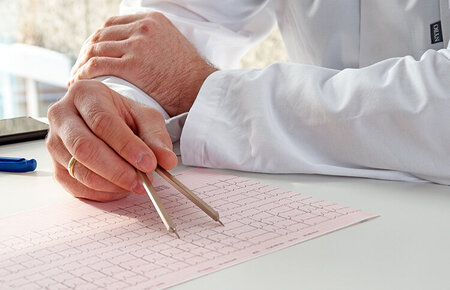 Hände eines Arztes, der ein auf dem Tisch liegendes EKG auswertet